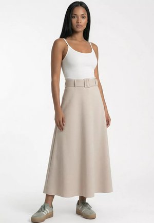 Kobieta w białej bluzce bez rękawów, beżowej spódnicy midi z paskiem i szarych sneakersach, stojąca na białym tle.