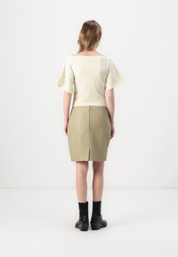 Lys beige topp med korte, utsvingte ermer; olivengrønn blyantskjørt; ankelhøye svarte hælboots; glatt tekstur; minimal design.