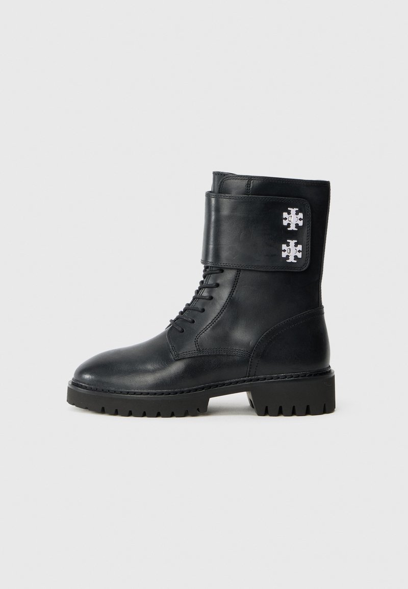 Czarne skórzane buty wojskowe z wiązaniem, z grubą podeszwą i szerokim paskiem, z dwoma metalowymi dekoracyjnymi logo po bokach.