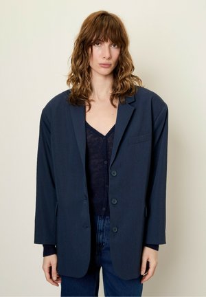 Námořnický oversized blazer se strukturovanými rameny, jedním knoflíkovým zapínáním a jemnými detaily kapes. Nositý přes tmavý, přiléhavý top.