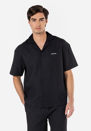 Camisa de botones de manga corta negra con una textura a rayas, que cuenta con un cuello puntiagudo y un pequeño logo blanco en el lado izquierdo del pecho.