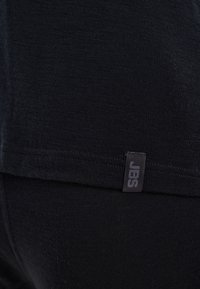 Sort t-shirt lavet af blødt bomuld, med rund halsudskæring, korte ærmer og et lille "JBS" logo tag i kanten.