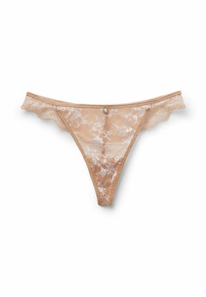 Stringt beige en dentelle avec motif floral et petite décoration en bijoux au centre avant sur fond blanc.