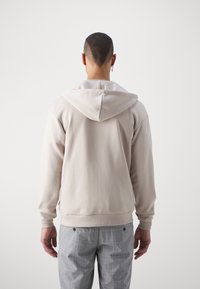 Felpa con cappuccio beige realizzata in tessuto morbido, caratterizzata da una vestibilità ampia e polsini a coste. Le cuciture visibili e il design semplice ne esaltano la minimalità.