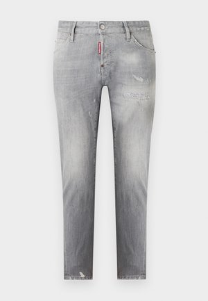 Jean gris slim avec effet délavé, légère usure subtile sur les cuisses et le genou, et une étiquette de marque rouge près de la poche avant.