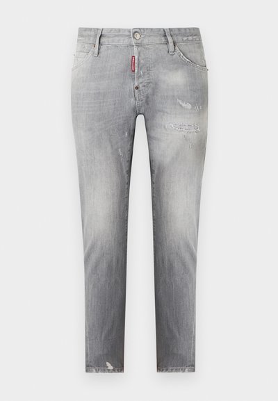 Jean gris slim avec effet délavé, légère usure subtile sur les cuisses et le genou, et une étiquette de marque rouge près de la poche avant.