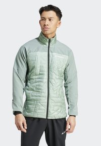 Chaqueta de color verde claro con cremallera, con textura acolchada en la parte frontal, mangas largas y cremalleras negras. Logo de la marca en la parte superior izquierda.