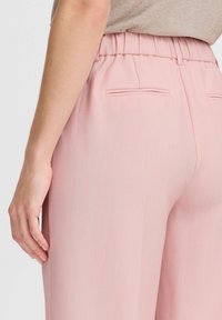 Pink wide-leg trousers with a textured finish, featuring an elastic waistband and two back pockets, shown from the side.