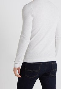 Ljusgrå tröja med långärmad och ribbad textur, kombinerad med mörkblå jeans med gul sömnad och detaljer på bakfickan.