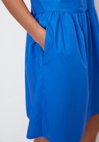 Abito blu con vita arricciata, tasca laterale e texture liscia con una leggera lucentezza, tagliato all'altezza del ginocchio.