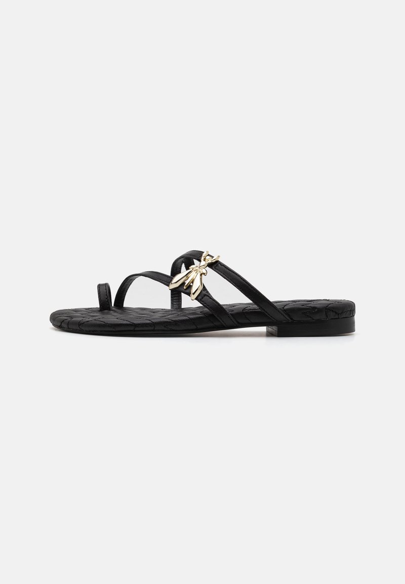 Svart platt sandal med vävd struktur, smala remmar och en dekorativ guldaccent. Enkel, öppen design med låg klack och minimalistisk stil.