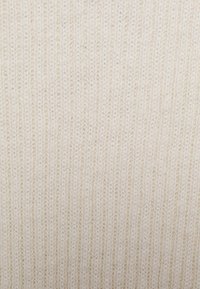 Tecido de malha creme com uma textura canelada, apresentando linhas verticais e uma aparência suave, adequado para vestuário ou têxteis para o lar.