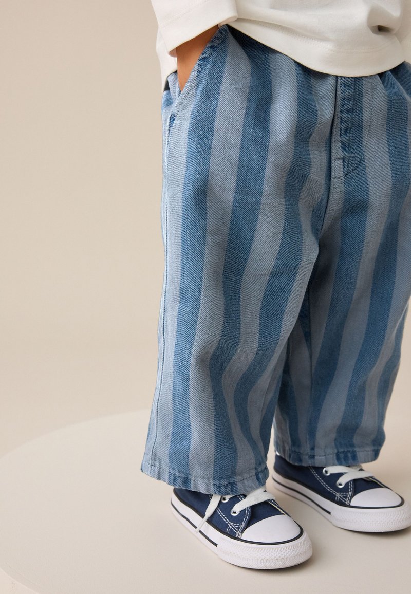 Blue striped denim pants with wide legs, featuring side pockets. Paired with dark blue sneakers with white rubber soles and laces.