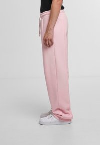 Pink sweatpants with an elastic waistband and drawstrings, featuring a straight leg design and a soft texture. Paired with white sneakers.