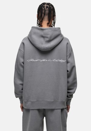 Grijze oversized hoodie met een capuchon. Heeft witte cursieve tekst "Good For Nothing" op de achterkant. Zacht, gestructureerd materiaal, relaxte pasvorm.