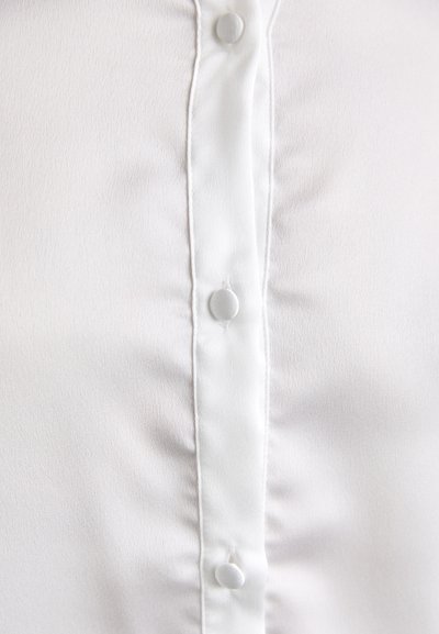 Blusa bianca con una texture liscia, caratterizzata da una patta centrale con bottoni rotondi e una sottile lucentezza su tutta la stoffa.