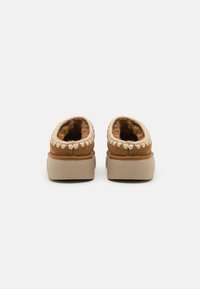 Brune fløyels slip-on sko med en beige, teksturert såle og kremfargede detaljer rundt åpningen. Myk, lodden innersåle synlig.