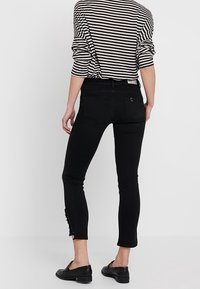 Svarta slim-fit jeans med medelhög midja, med sidoflikar vid anklarna och ett mjukt, stretschigt tyg. Kombinerat med en randig topp.