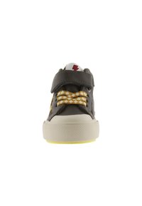 Black and white children's sneaker with yellow checkered laces, a velcro strap, and a red lightning bolt on the tongue, shown from the front.