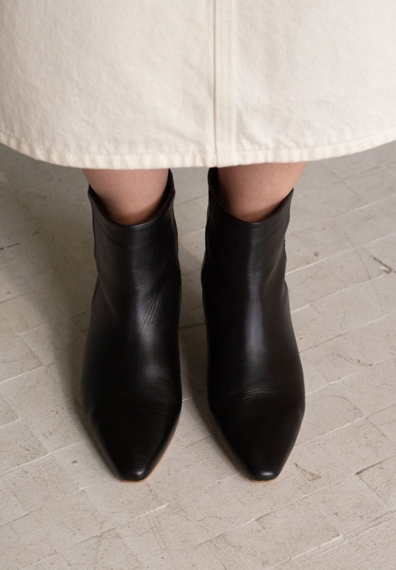 Juodi odiniai aulinukai su smailia nosimi ir lygiu paviršiumi, parodyti iš viršaus ant šviesios, struktūruotos grindų dangos.