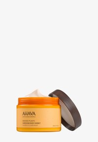 Orange rund burk med ett mörkbrunt lock, innehållande krämfärgad kroppssorbet. Etiketten har svart text på en ljus bakgrund.