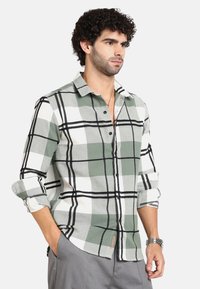 Camicia a quadri verde e bianca con dettagli neri, maniche lunghe, apertura con bottoni, realizzata in tessuto texturizzato. Presenta maniche arrotolabili e tag con logo.