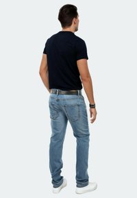 Blaue Denim-Jeans mit geradem Schnitt, sichtbaren Nähten, zwei Gesäßtaschen und einem schwarzen Gürtel, kombiniert mit einem dunklen T-Shirt und weißen Sneakers.