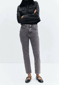 Chaqueta de cuero negra corta con cuello de piel sintética, combinada con jeans de denim gris de talle alto y zapatos planos negros. El conjunto es casual y ajustado.