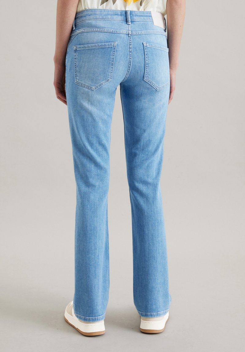 Jasnoniebieskie dżinsy z szerokimi nogawkami z denimu, z dwoma tylnymi kieszeniami i średnim stanem, połączone z białymi trampkami.