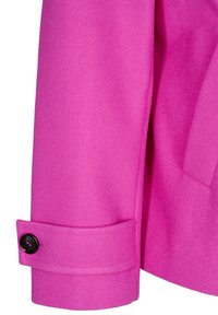 Manche de manteau rose vif avec un poignet maintenu par un seul bouton noir et une poche latérale visible sur le vêtement.