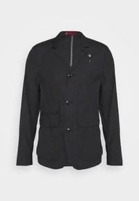 Svart lättviktsjacka med en strukturerad design, två framfickor, en bröstficka och knappstängning. Har subtil textur och detaljer.