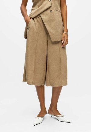 Beige, strukturierte Culottes mit lockerer Passform und Seitentaschen, kombiniert mit weißen Mules mit spitzem Zehenbereich und kleinem Absatz.