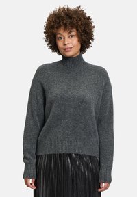 Dunkelgrauer, gestrickter Rollkragenpullover mit gerippten Bündchen und Saum, kombiniert mit einem plissierten, metallischen Rock. Weiche Textur und lockere Passform.