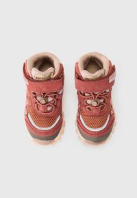 Des sneakers pour enfants rouges et bruns en matériau en maille et en daim, dotés d'une bride Velcro, de lacets élastiques et d'une semelle texturée pour l'adhérence.