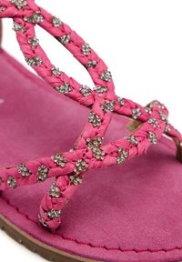 Sandalia rosa con correas trenzadas que presentan adornos metálicos. Suela suave, con textura similar al ante, en un tono rosa a juego. Diseño de punta redonda.