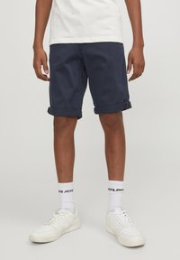 Pantaloni corti blu navy in cotone, con orli arrotolati e due tasche laterali, abbinati a sneaker bianche e calze con scritte nere.
