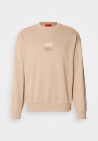 Sweatshirt beige à col rond avec poignets et ourlet côtelés, présentant un petit logo carré bicolore "HUGO" centré sur la poitrine.