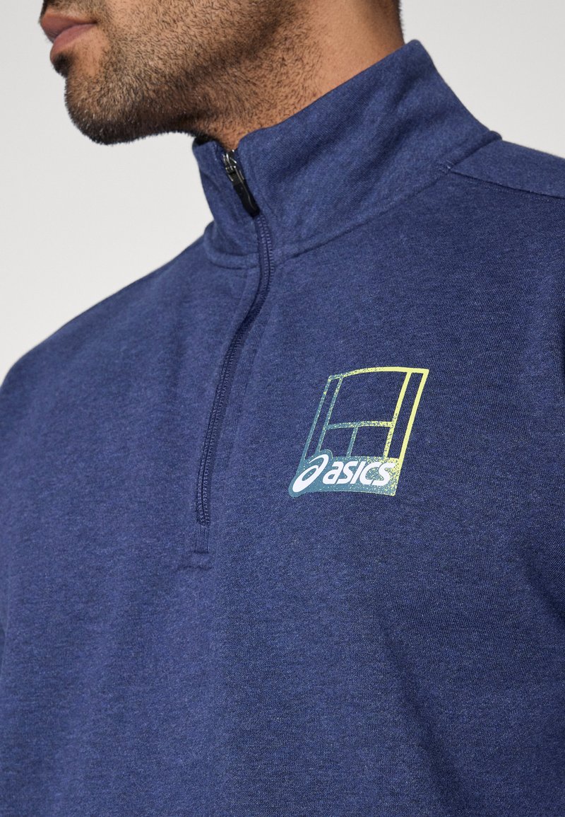 Pull-over en polaire bleu marine à fermeture éclair sur le quart supérieur, avec une finition texturée, arborant un logo multicolore sur le côté gauche de la poitrine.