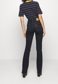 Jean taille haute bleu marine avec une coupe droite, couture contrastante et deux poches arrière avec un design courbé distinctif.