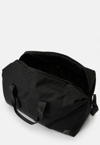 Black duffel bag made of durable fabric, with a wide opening, two sturdy handles, and a detachable shoulder strap. Inside is lined.