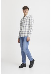 Plaid button-up shirt in white and gray, long sleeves, paired with light blue jeans and black lace-up shoes, on a plain background.