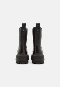Botas negras hasta el tobillo con un acabado brillante, que cuentan con una suela gruesa, lengüetas para ponerlas fácilmente y un destacado logo "BUFFAL" en los lados.