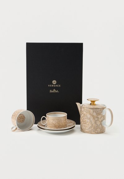 Πολυτελές σετ τσαγιού από πορσελάνη σε μπεζ και χρυσό με λουλουδάτο σχέδιο, που περιλαμβάνει τσαγιέρα, δύο φλυτζάνια, πιατάκια και μαύρο κουτί με το λογότυπο Versace Rosenthal.