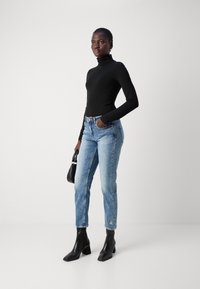 Schwarzes Rollkragenoberteil, hellblaue gerade Jeans mit floralem Bestickungsdetail und schwarze Ankle Boots mit quadratischer Zehenform.