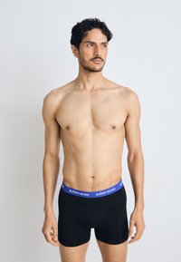Fekete boxer alsónadrág kék derékkal, amelyen a "BJÖRN BORG" felirat található. A modell semleges arckifejezéssel áll, egy sima háttér előtt.