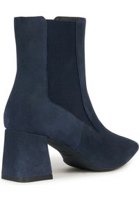 Stivale alla caviglia blu navy con punta affusolata e tacco spesso, caratterizzato da una combinazione di suede e pannelli elasticizzati. Texture liscia e cuciture minime.