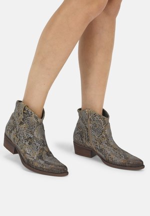 Stivaletti in pelle con motivo effetto pelle di serpente fino alla caviglia con tacchi bassi a blocco, indossati su gambe nude su sfondo semplice.