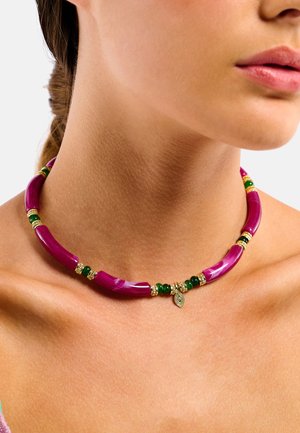 Des perles tubulaires violettes entrecoupées d'accents verts et dorés forment un collier ras-du-cou, orné d'un petit pendentif en forme de feuille.