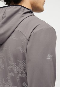 Γκρι κασκόλ με λείο υφασμάτινο ύφασμα, με διακριτικό καμουφλάζ και μικρό αντανακλαστικό λογότυπο στο μανίκι.