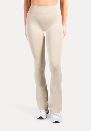 Leggings acampanados beige con una cintura alta, confeccionados en una tela lisa y elástica. Presentan un diseño minimalista sin estampados ni accesorios visibles.